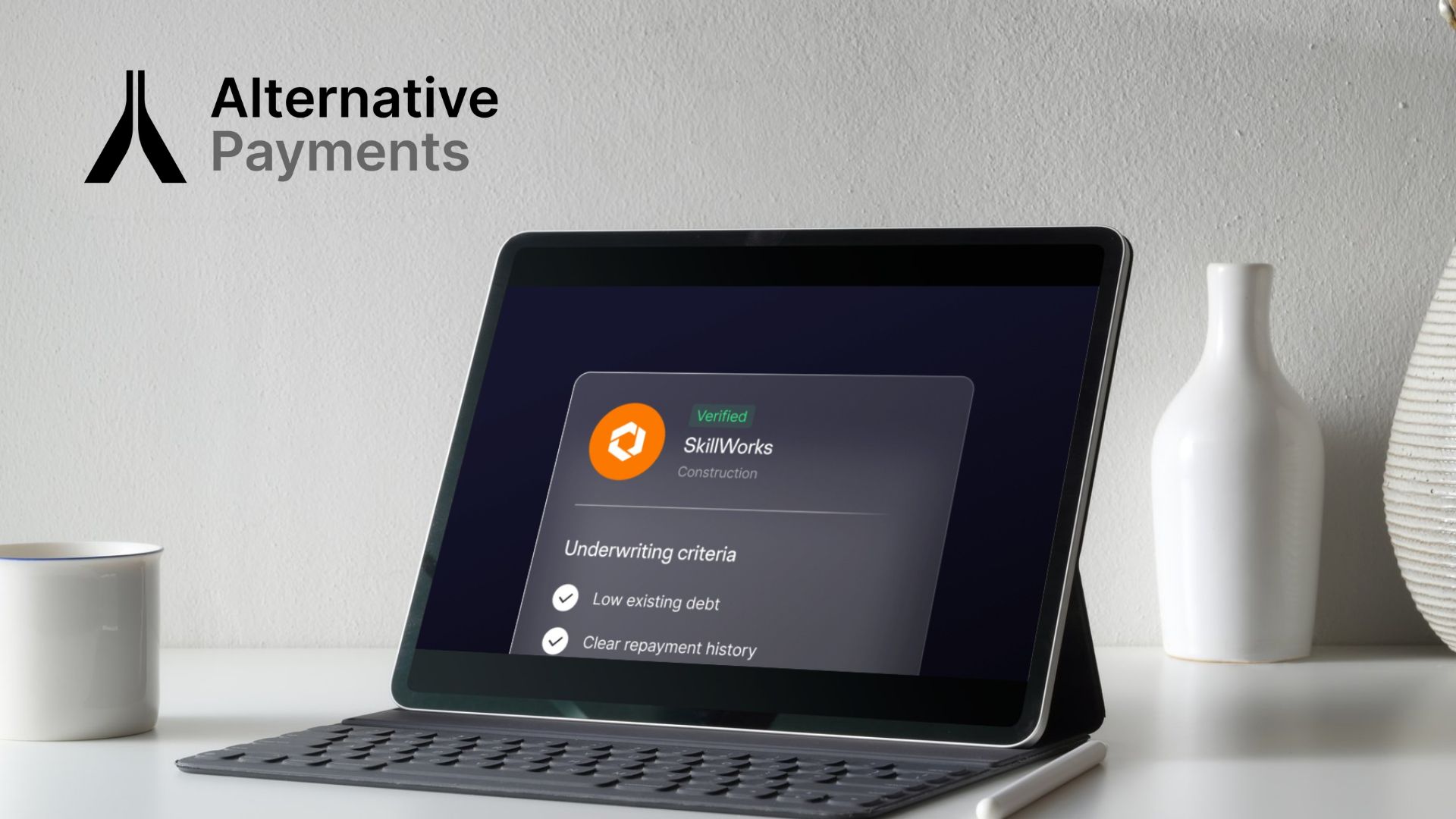 A graphic of a tablet with a detachable keyboard showing approved financing for a business looking for flex payment terms. The tablet is set on a kitchen counter with a coffee mug and vase next to it. The Alternative Payments logo in black and grey is located in the left upper middle of the landscape image.